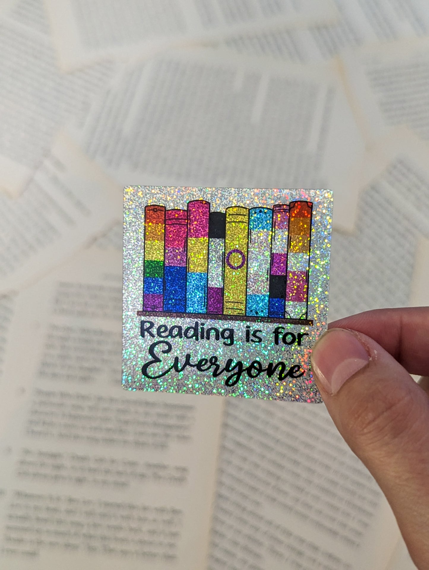 A set of 8 books sitting on a shelf. The books are each a different pride flag. From left to right Rainbow, Bisexual, Pansexual, Asexual, Intersex, Transgender, Genderfluid, Lesbian. The whole sticker is sparkly